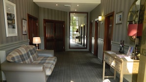 Une chambre d’hôtel avec un canapé, un bureau et une lampe. Un couloir mène à une autre pièce.