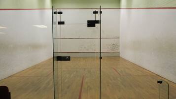 A squash court with glass doors, wooden floor, and white walls.