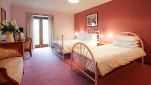 Une chambre d’hôtel avec deux lits, un bureau avec une chaise, une grande fenêtre avec des rideaux et un tableau au mur.