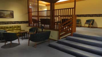 A staircase with a wooden railing, a green leather sofa, and plaid chairs in a room with a carpeted floor.