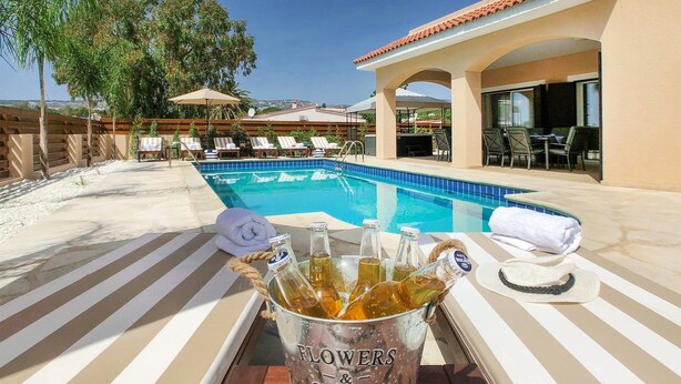 A poolside area with lounge chairs, a pool, and a bucket of drinks. - Villa Sapphire (Paphos)