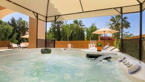 A hot tub with a wooden deck and lounge chairs, surrounded by palm trees and a clear sky. - Villa Sapphire (Paphos)