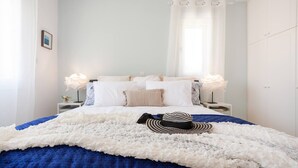 A neatly made bed with white linens, a blue blanket, and a striped hat on the bed. - Villa Sapphire (Paphos)