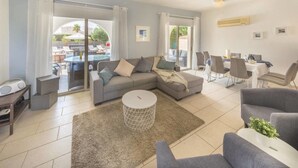 A modern living room with a grey sofa, a coffee table, and a dining area with chairs and a table. - Villa Maria (Pegeia)