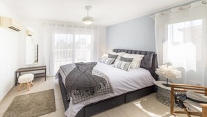 A modern bedroom with a large bed, a small side table, a bench, and a window with sheer curtains. - Villa Maria (Pegeia)