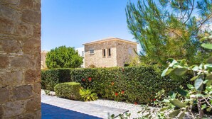 A stone building with a tiled roof, surrounded by a well-maintained garden with hedges and flowering plants. - Villa Maria (Pegeia)