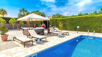Un espace piscine comprenant des chaises longues, un jacuzzi et une pergola.