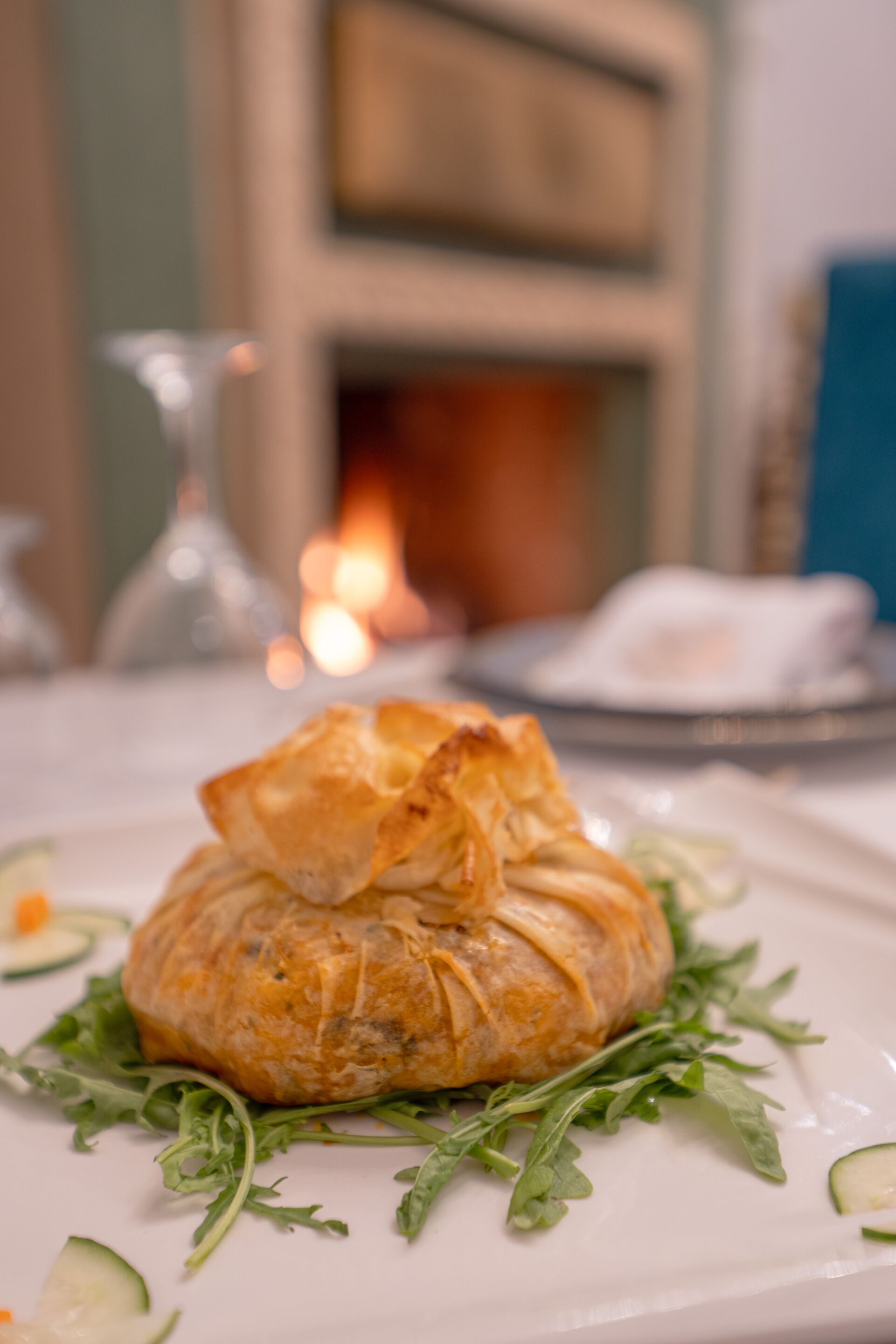 A plate with a pastry on a bed of greens, a candle, and a vase in the background.