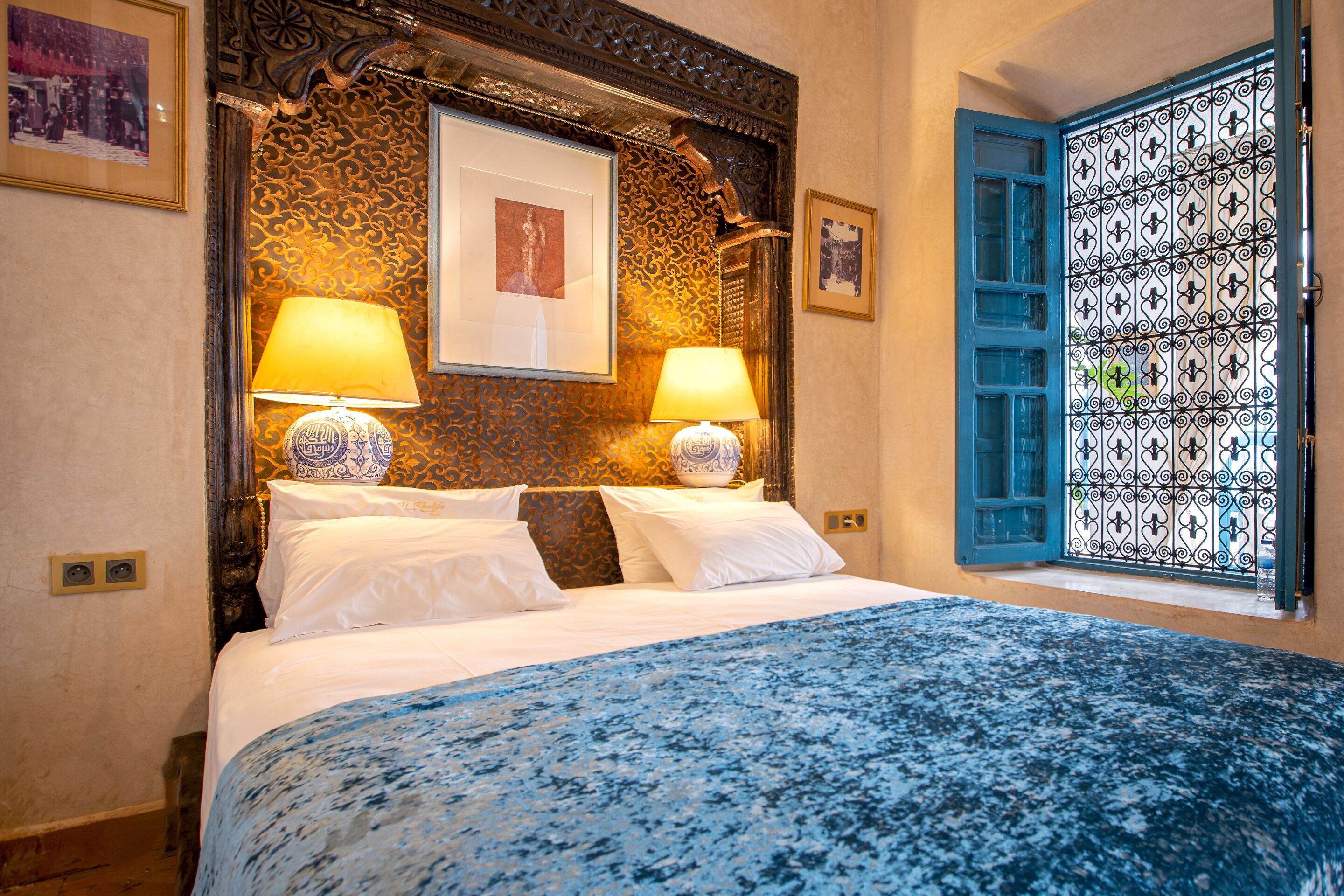 A bed with a blue patterned bedspread, two bedside lamps, and a decorative headboard.