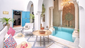 A pool area with a blue door, a white chair, and a table with a decorative item. - Riad Khalifa (Marrakech)