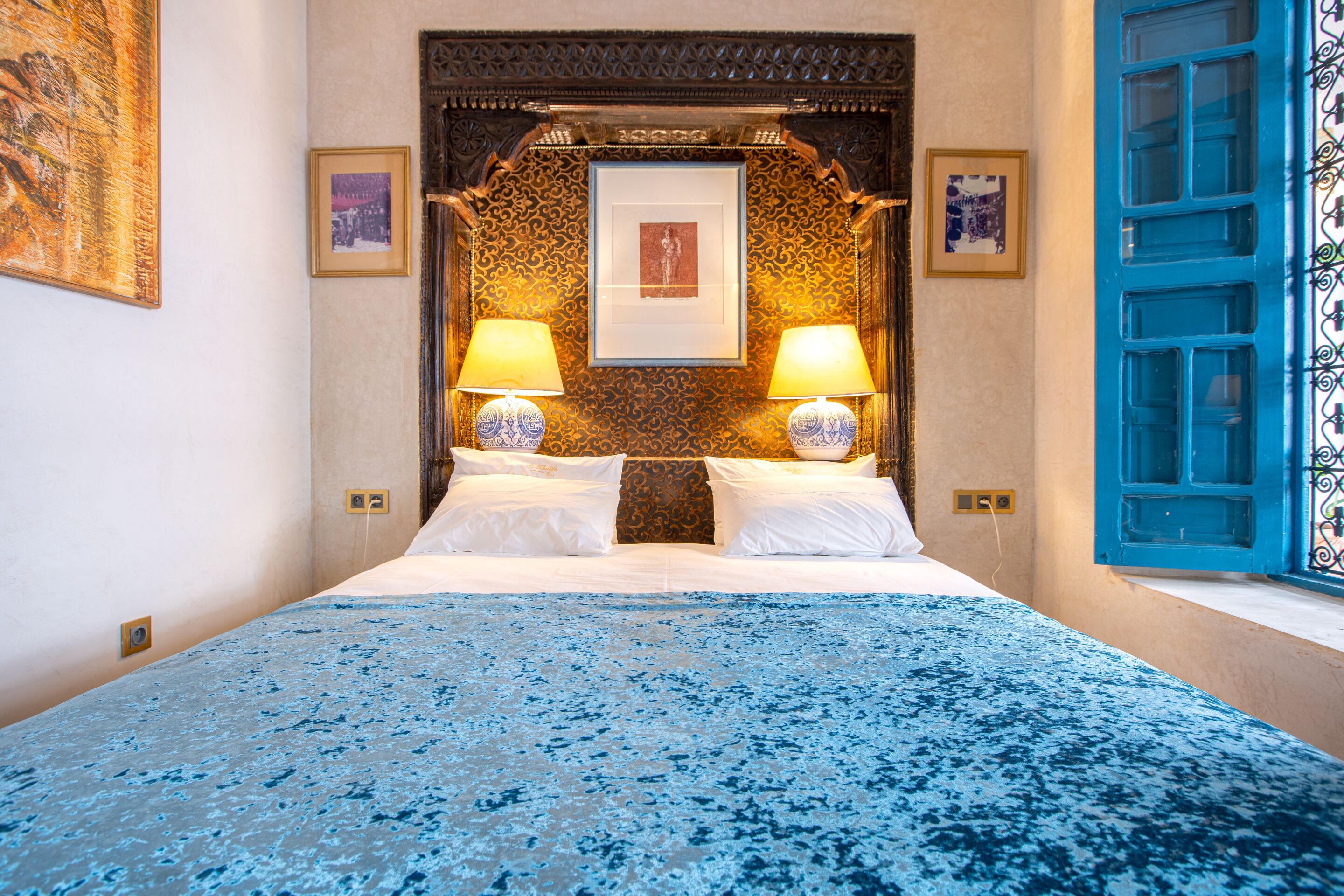 A bedroom with a bed, two bedside lamps, a framed picture above the bed, and a blue door.
