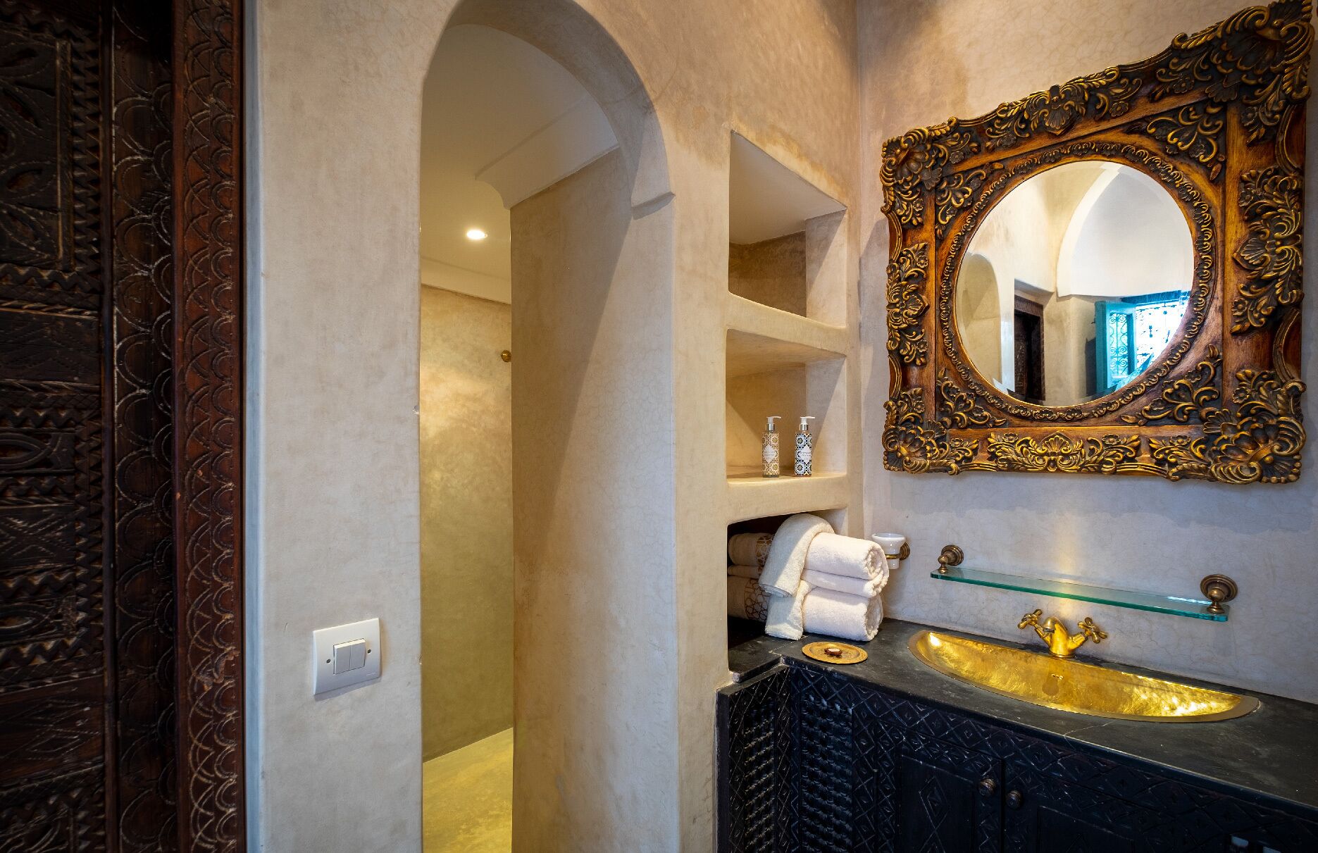 A bathroom with a gold sink, ornate mirror, and a towel rack.