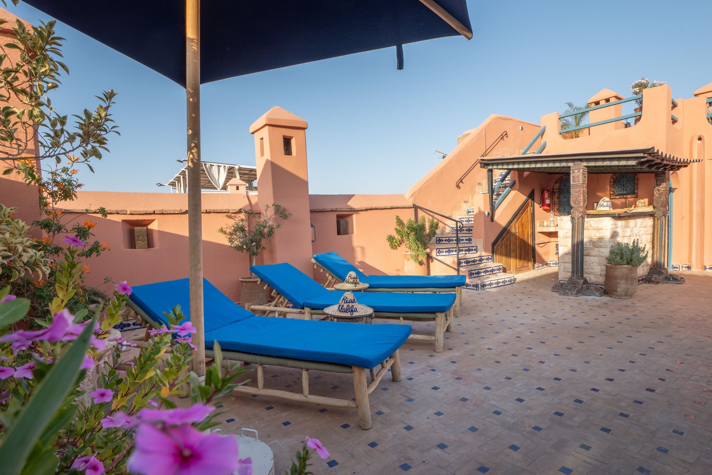 A courtyard with lounge chairs, a shaded area, and a building with a tower.