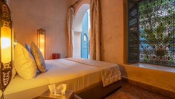 A bedroom with a bed, a nightstand, a lamp, a window with a view, and a door with a decorative screen.