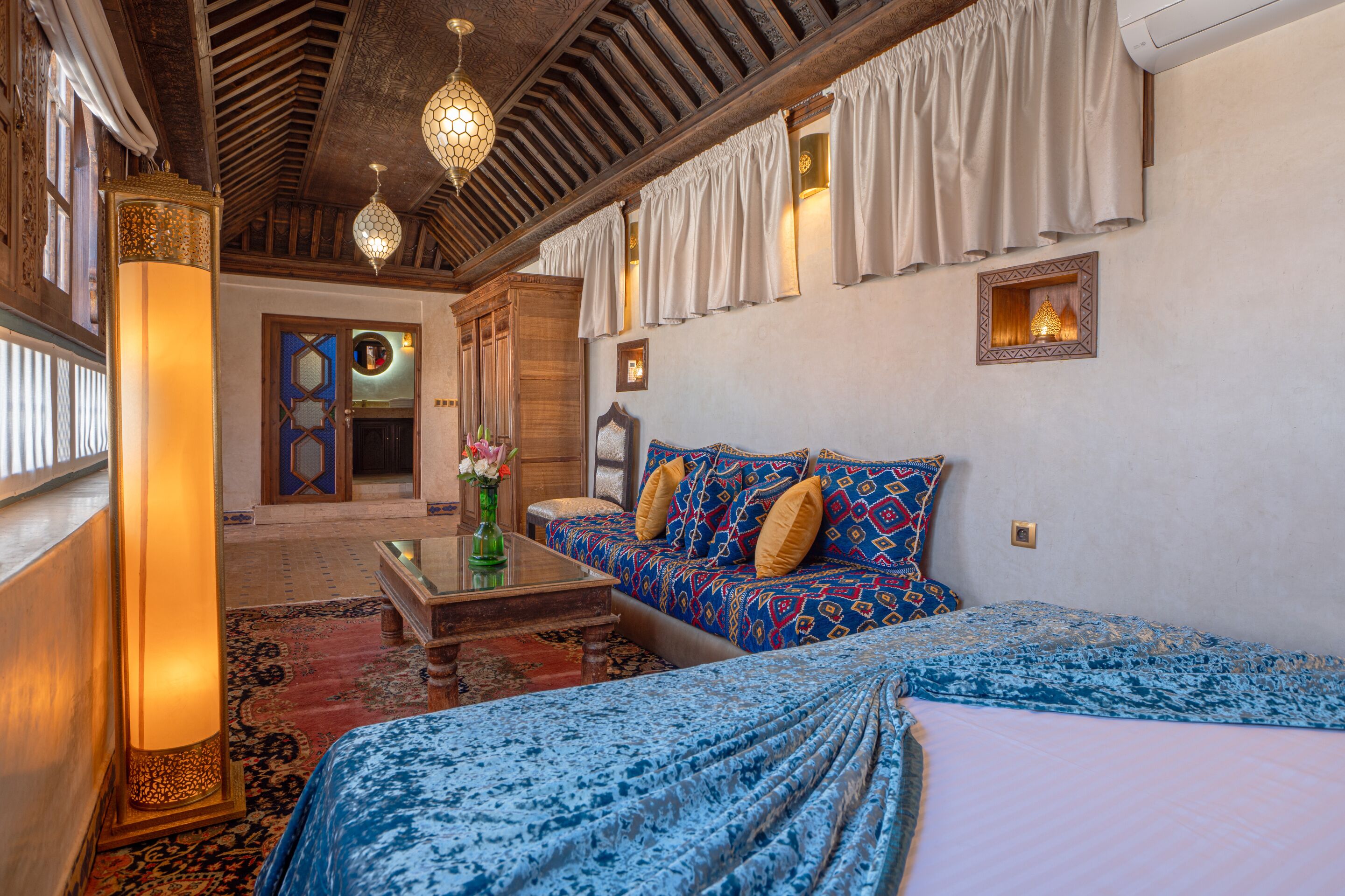 Quarto tradicional com sofá, cama, mesa de centro e uma luminária decorativa.