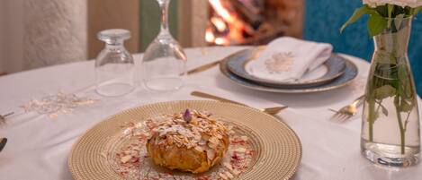 Una mesa de comedor con un plato de comida, un jarrón con flores y una chimenea al fondo.