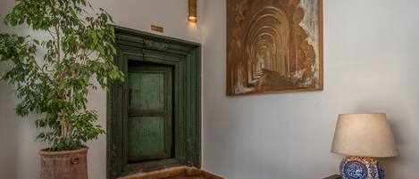 Un pasillo con una puerta verde, una planta en maceta, una lámpara y un cuadro decorativo en la pared.