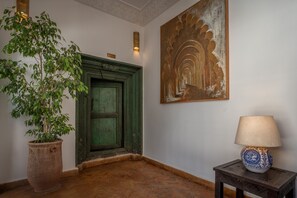 A hallway with a green door, a potted plant, a lamp, and a wall with a decorative painting. - Riad Khalifa (Marrakech)
