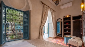 A room with a bed, a small table with a tray, a blue chair, and a decorative door with blue shutters. - Riad Khalifa (Marrakech)