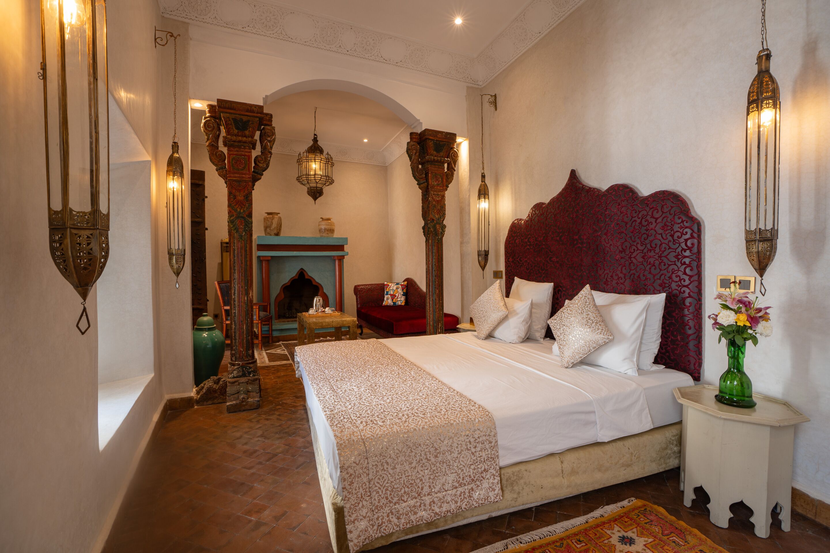 A bedroom with a large bed, ornate wall sconces, and a decorative fireplace.
