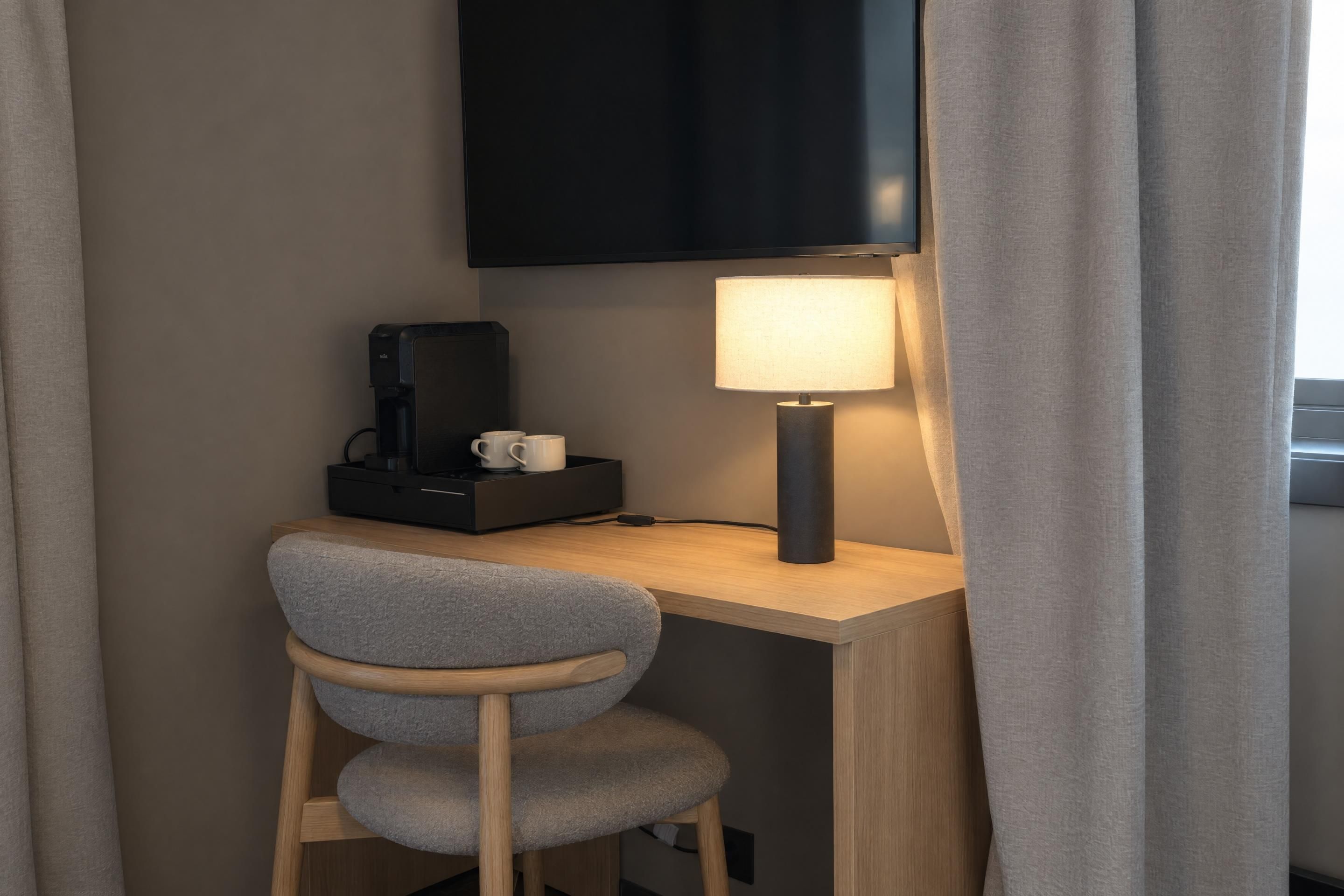 Een klein bureau met een stoel, een lamp en een koffiezetapparaat.