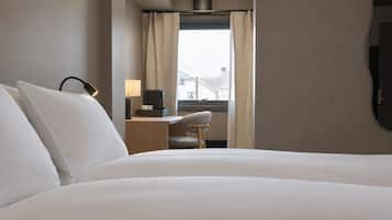 A hotel room with a bed, a desk with a lamp, a chair, and a window with curtains.