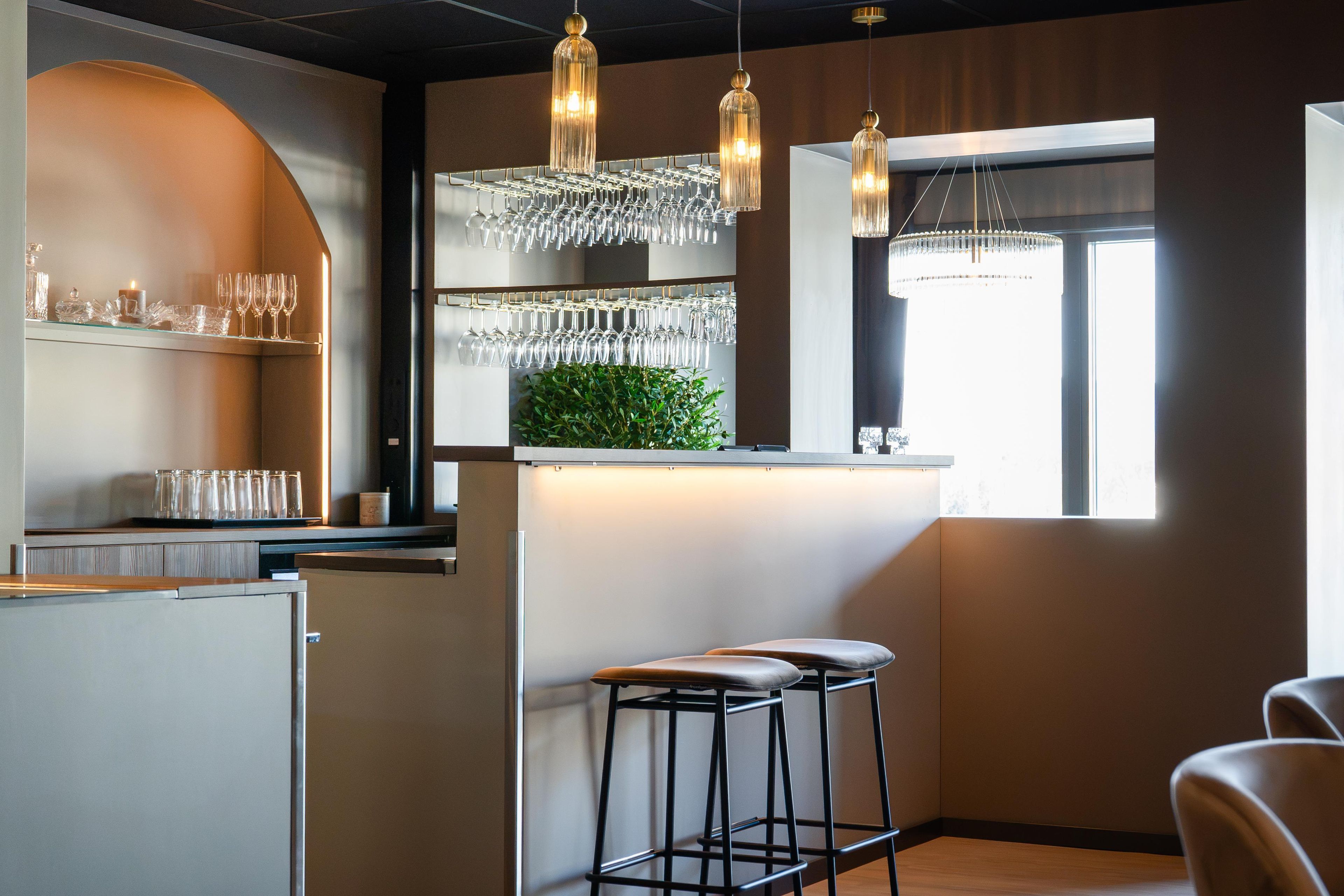 Een bar met krukken, een wijnrek en hangende lampen.