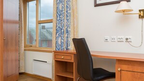 A room with a wooden desk, a black chair, a window with patterned curtains, a wall-mounted lamp, and a framed picture. - Best Western Hotel Alta (Alta)
