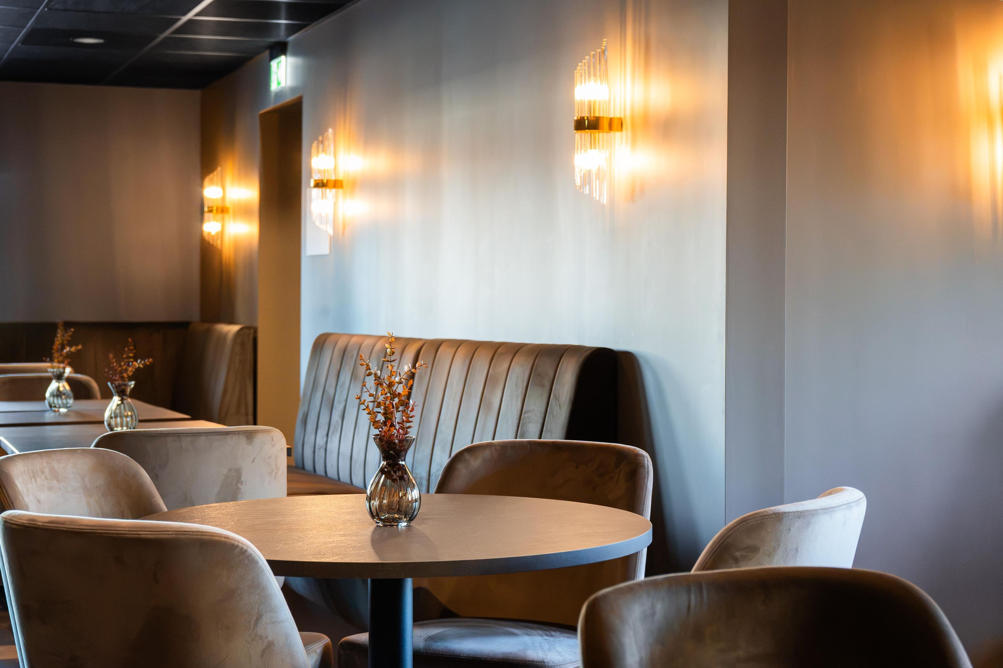 Een restaurantinterieur met ronde tafels, gestoffeerde zithoeken en wandlampen.