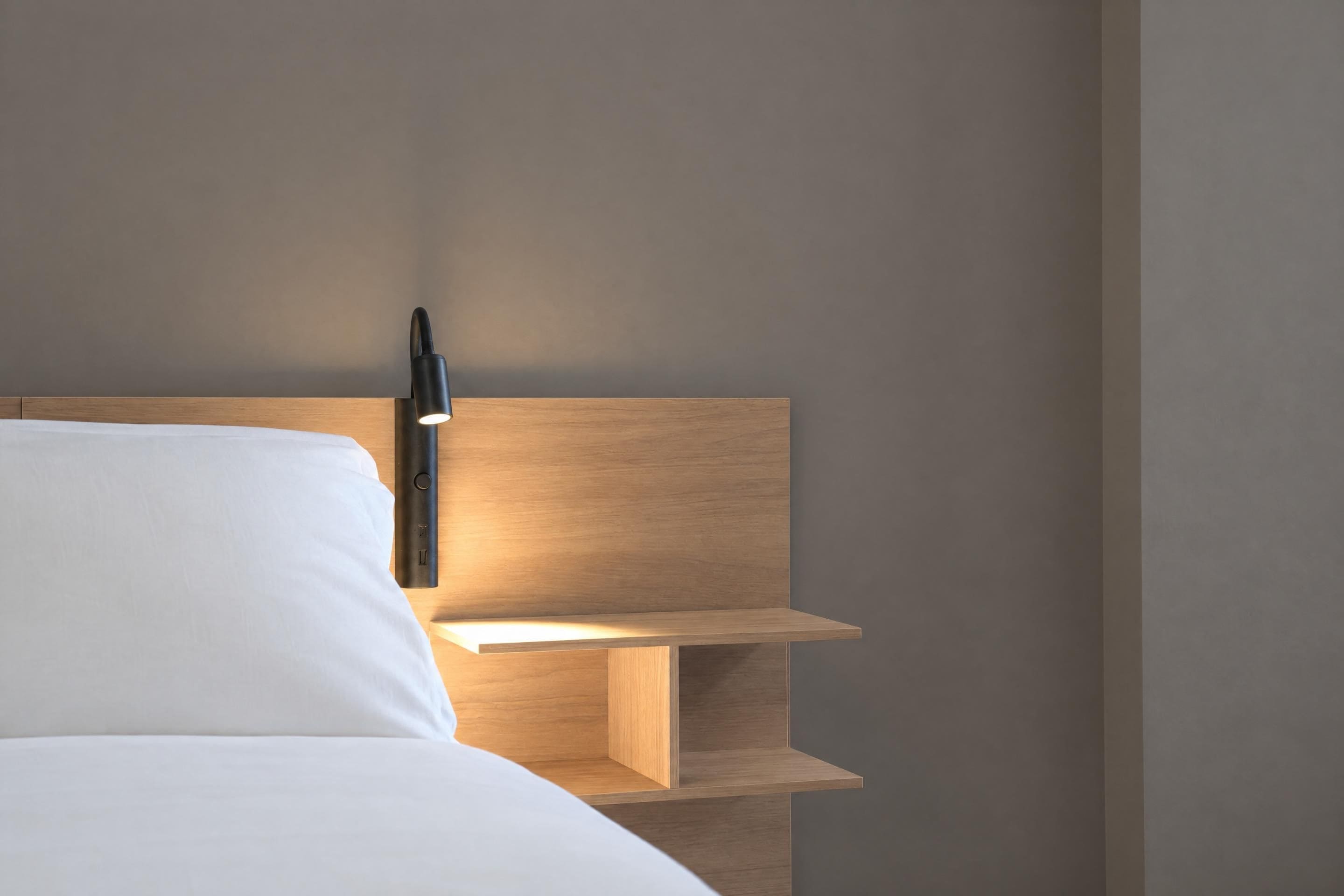 Una cama con cabecera, una mesita de noche y una lámpara de pared.