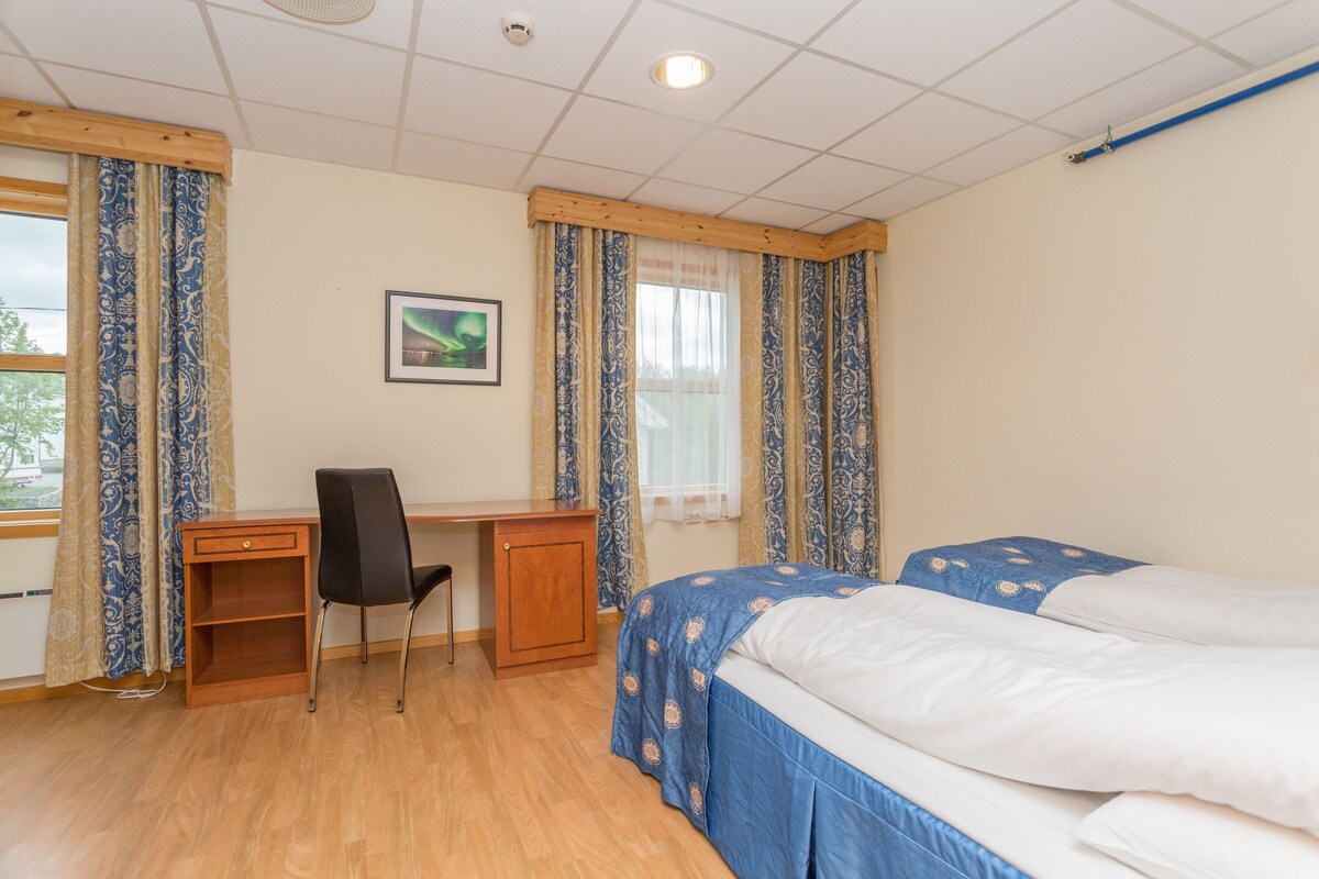 A bedroom with a desk, two beds, and a window with curtains.