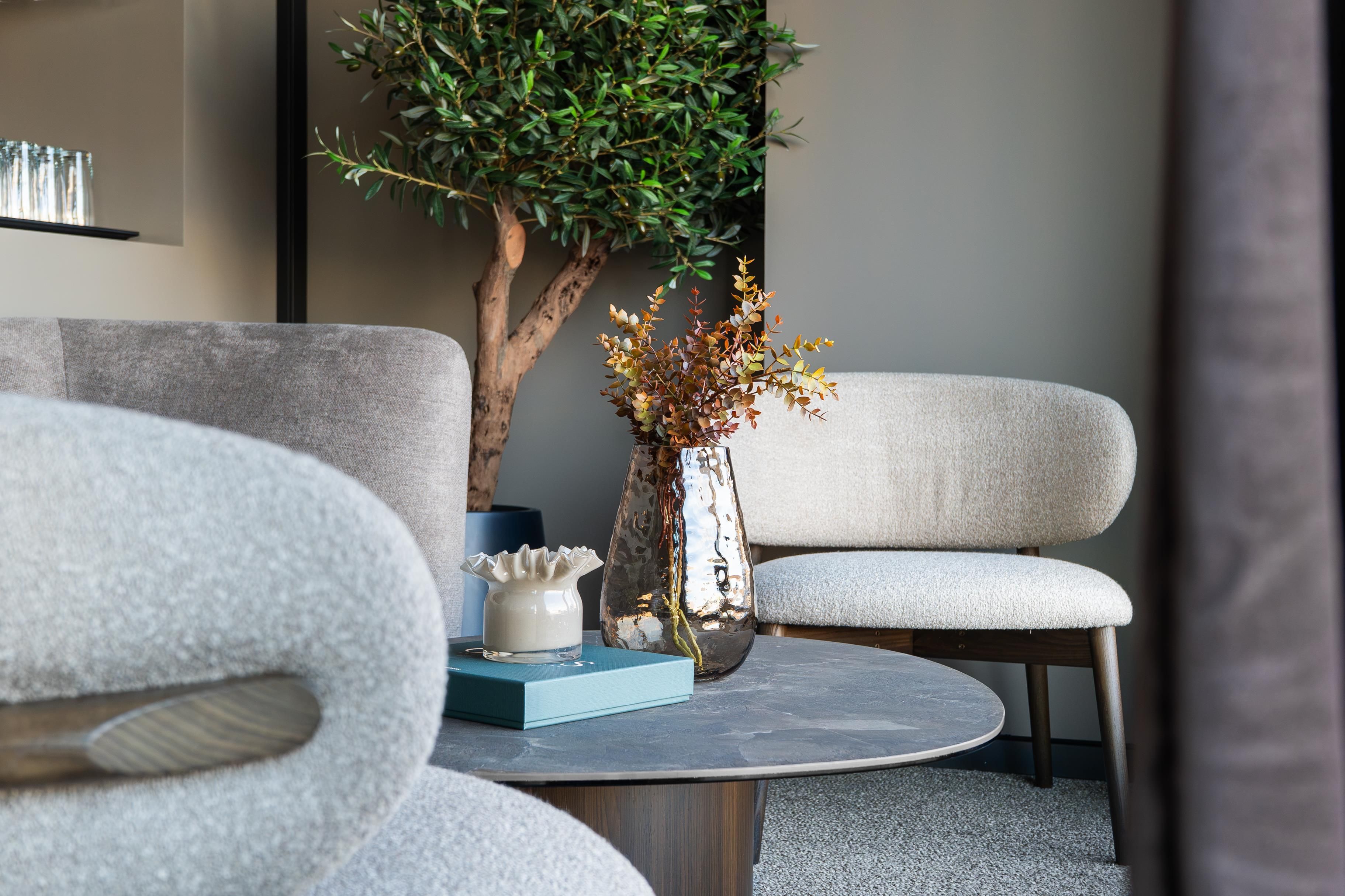 Una sala moderna con una mesa redonda, dos sofás grises, una planta en maceta y un jarrón decorativo.
