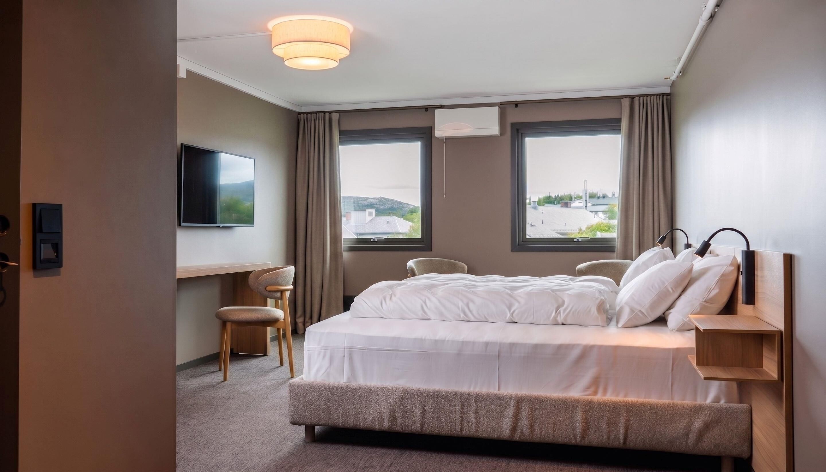 Habitación de hotel con cama, escritorio, silla, televisión y ventanas con vistas.
