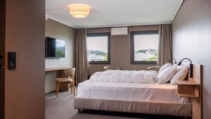 Habitación de hotel con cama, escritorio, silla, televisión y ventanas con vistas.