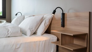 Una cama con ropa blanca y dos lámparas negras fijadas a la pared.
