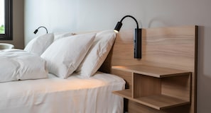 Una cama con ropa blanca y dos lámparas negras fijadas a la pared.