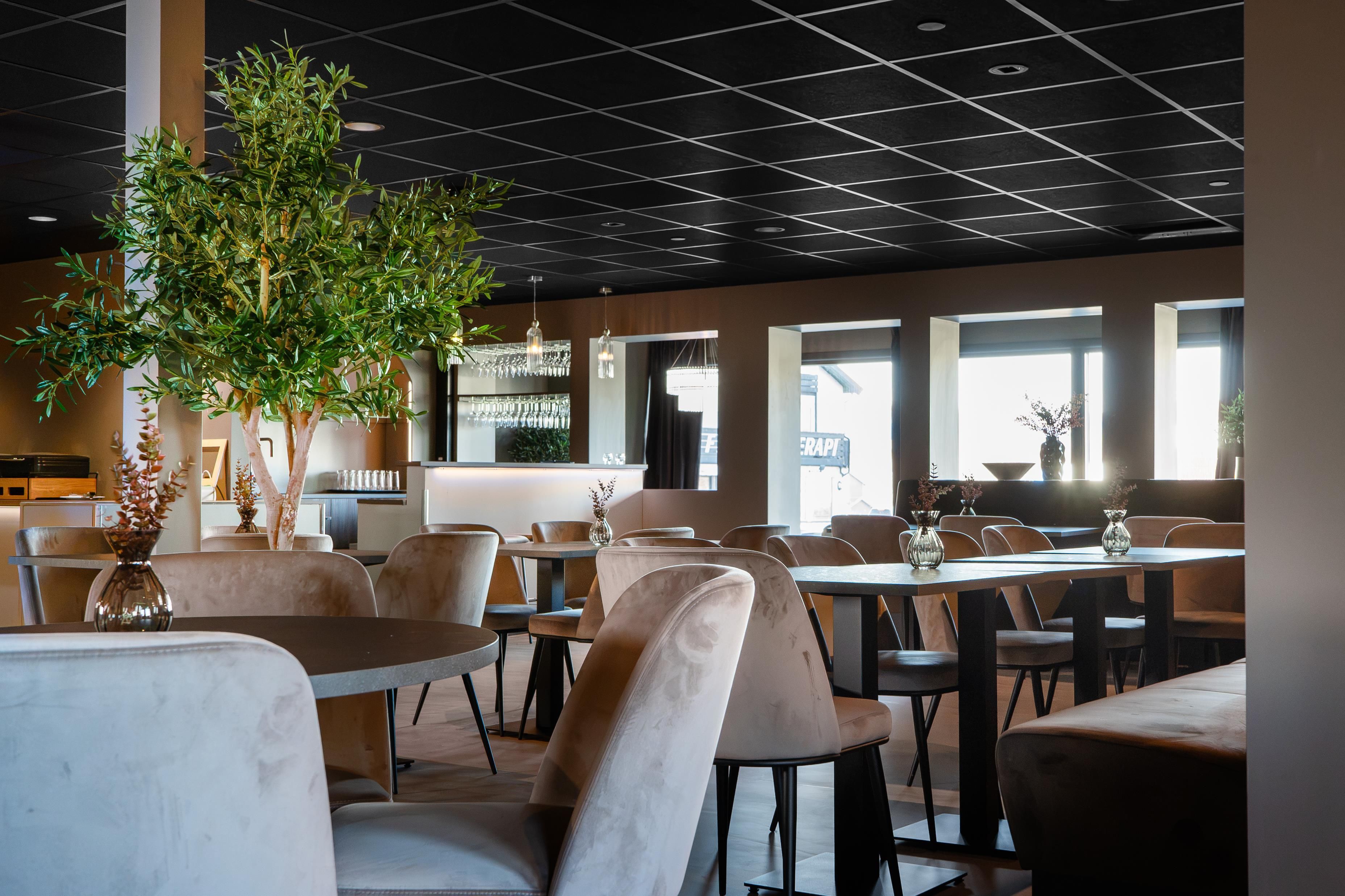 Un interior de restaurante moderno con mesas redondas, sillas acolchadas y una gran planta de interior.