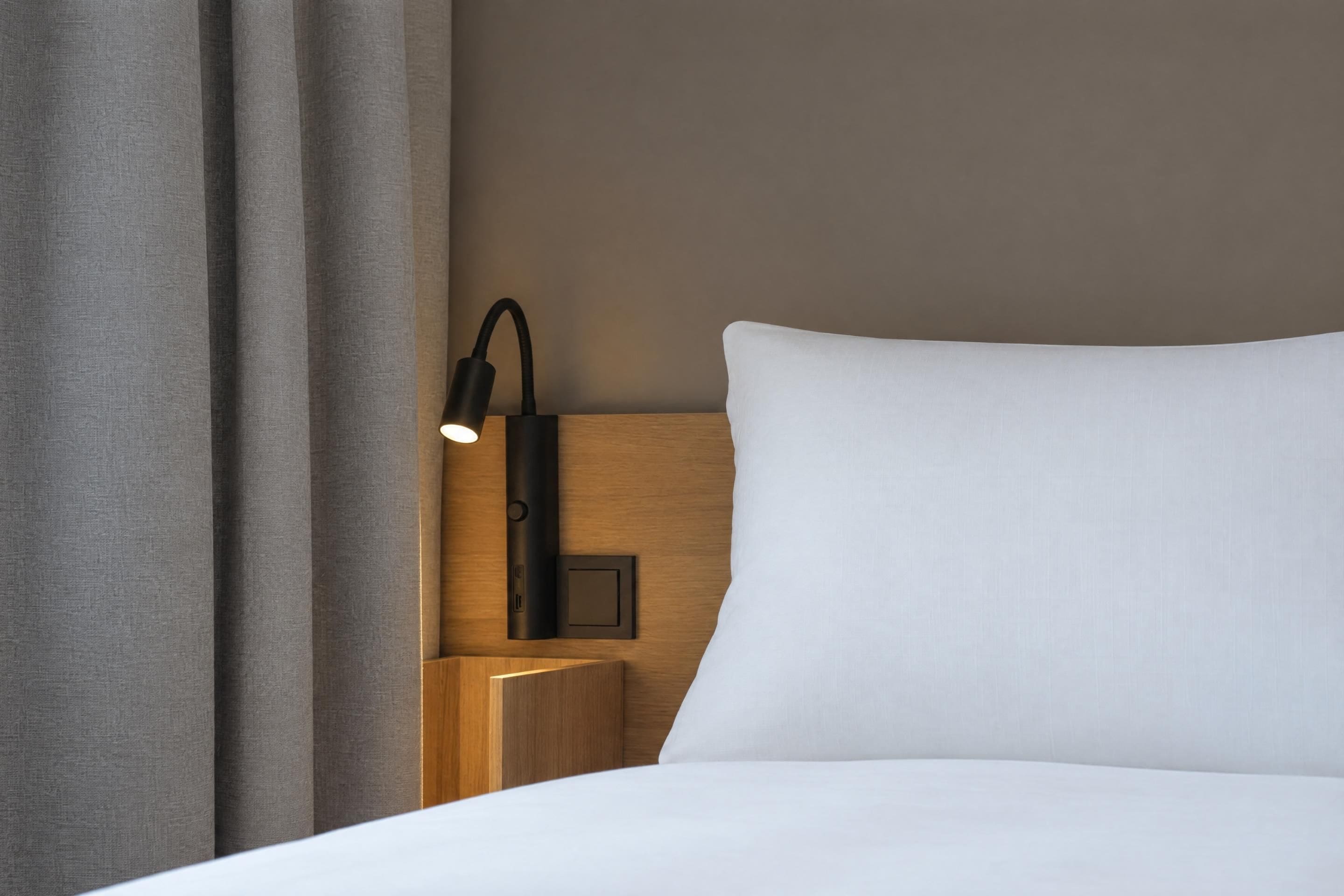 Un lit bien fait, avec un oreiller blanc et une tête de lit dotée d’un luminaire intégré.