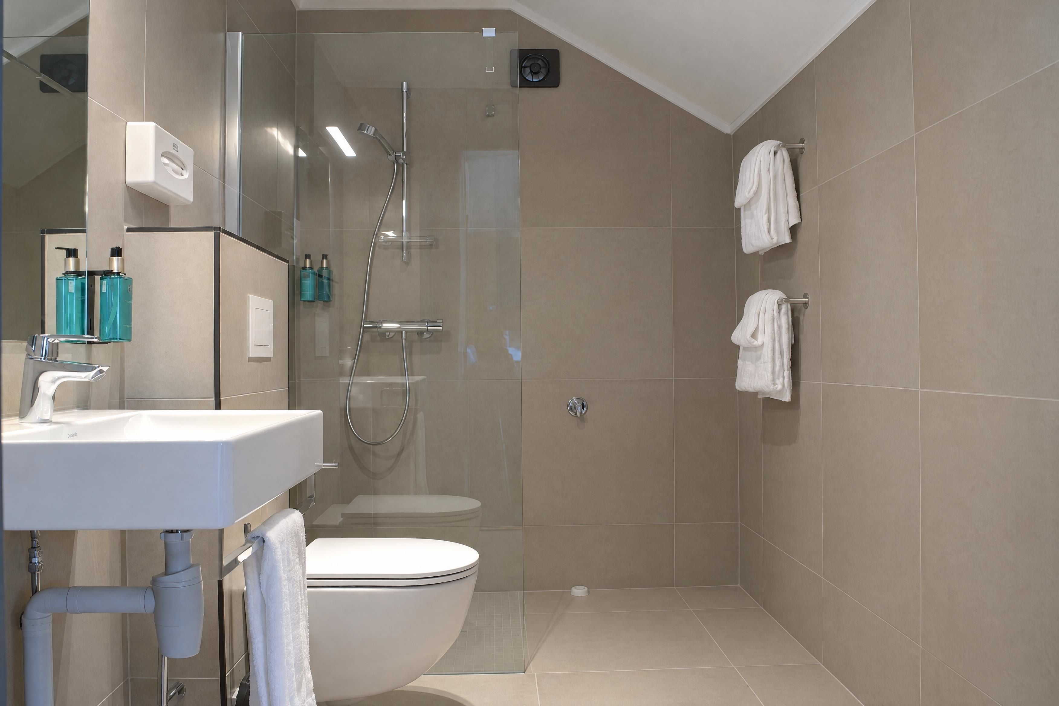 Un baño moderno con ducha envuelta en vidrio, inodoro y lavamanos con artículos de aseo.