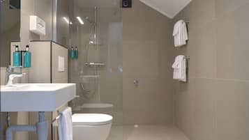 Un baño moderno con ducha envuelta en vidrio, inodoro y lavamanos con artículos de aseo.