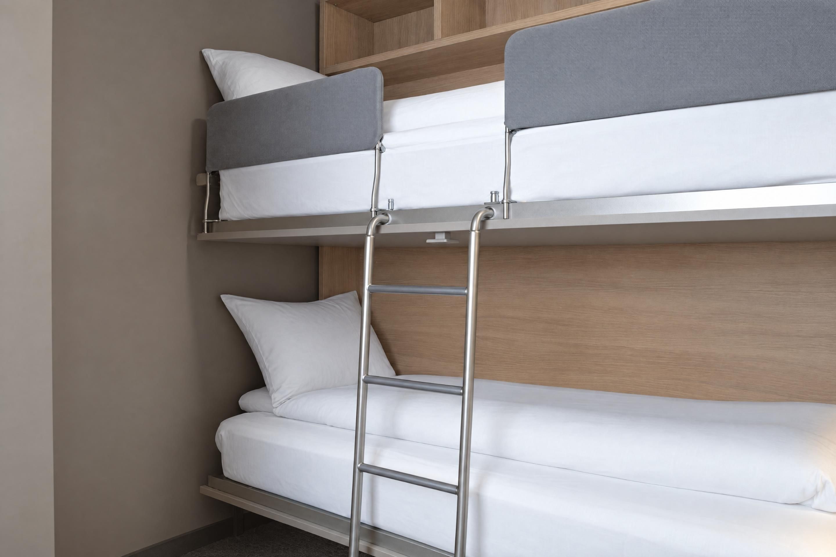 Una cama litera con escalera, ropa de cama blanca y cabecera de madera.