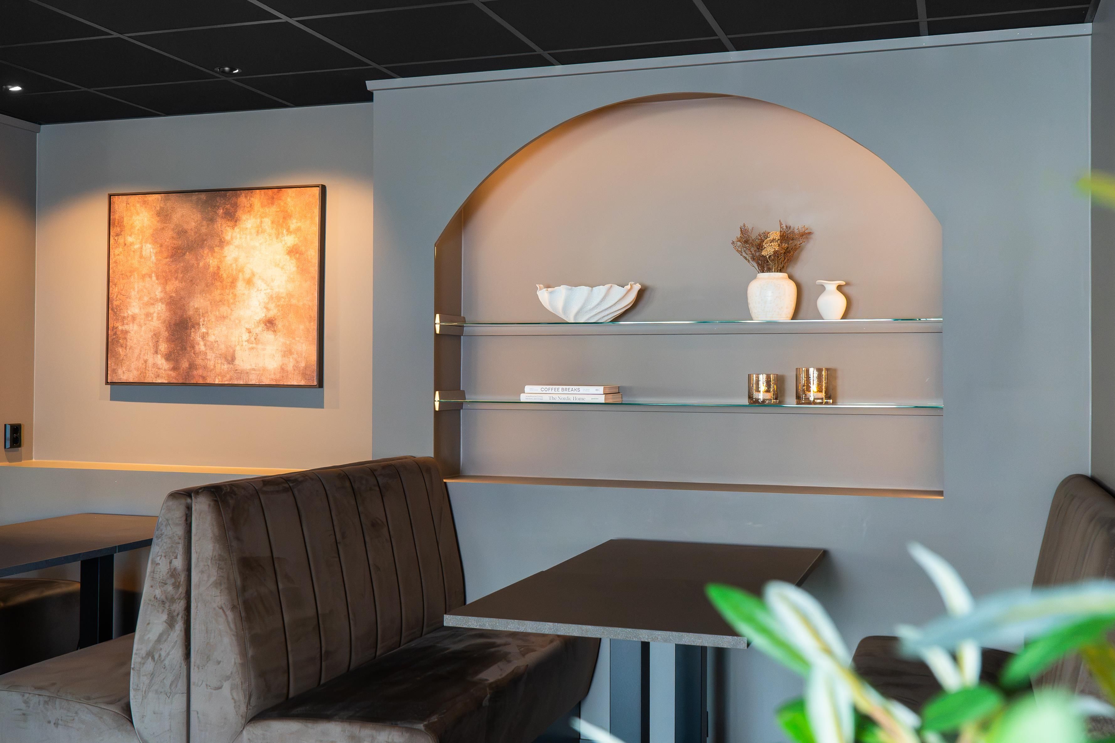 En modern inredning med en sittgrupp, ett glasbord och en vägghylla med dekorativa föremål.