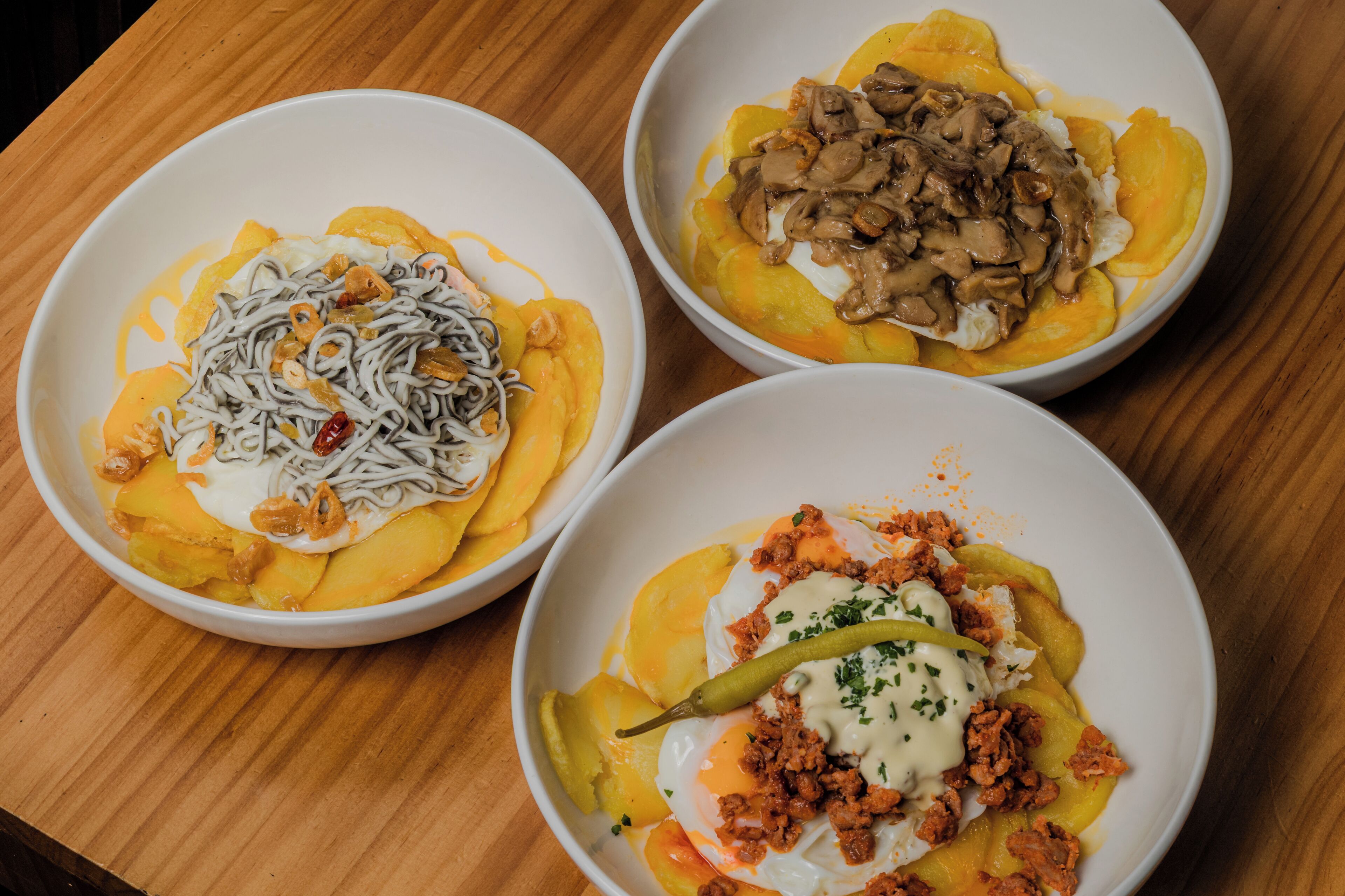 Three bowls of food with different toppings on a wooden table.