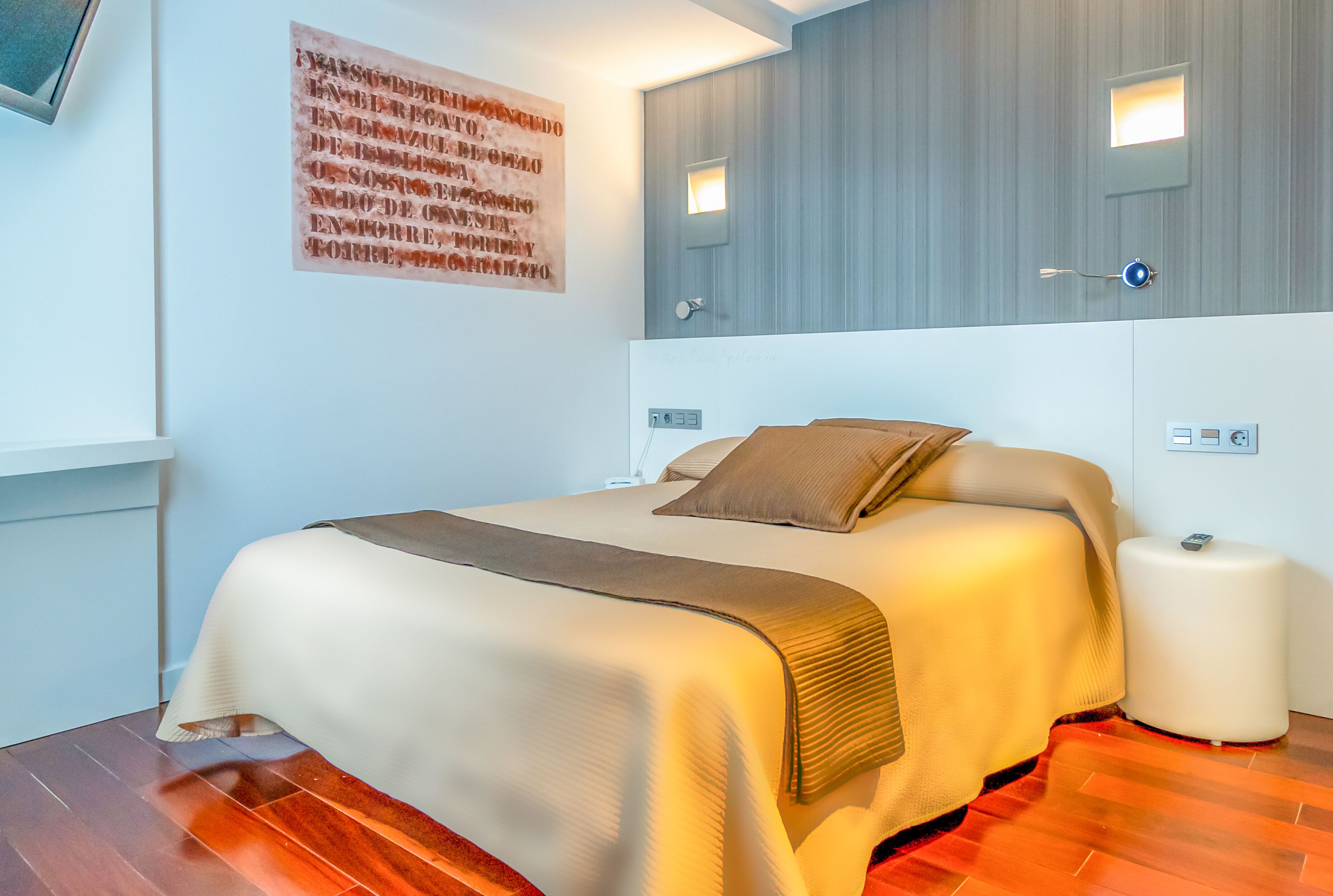 Een moderne hotelkamer met een groot bed, een nachtkastje, een spiegel aan de muur en een kleine bedlamp.