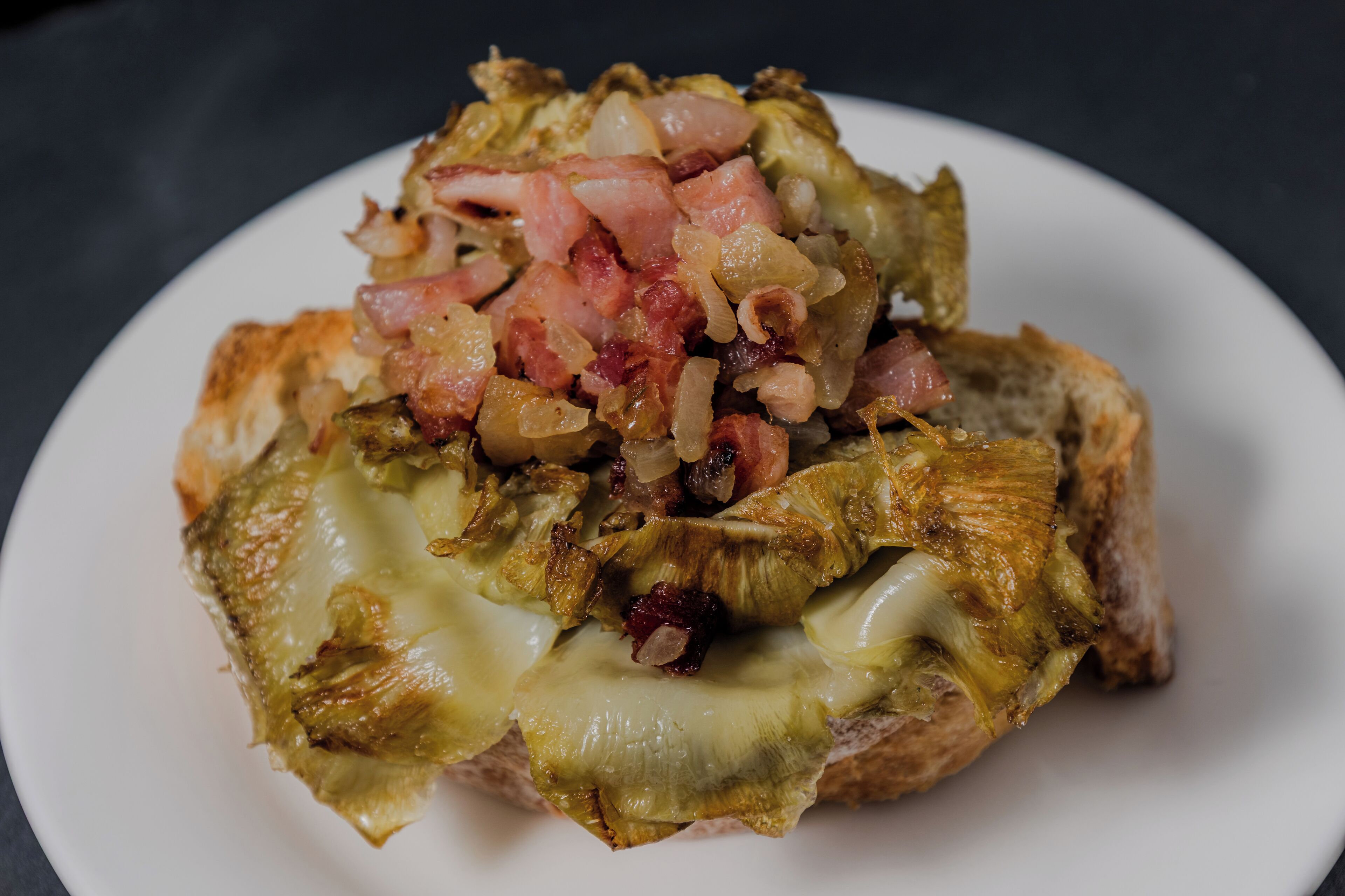 A plate with a sandwich topped with cheese, onions, and bacon.