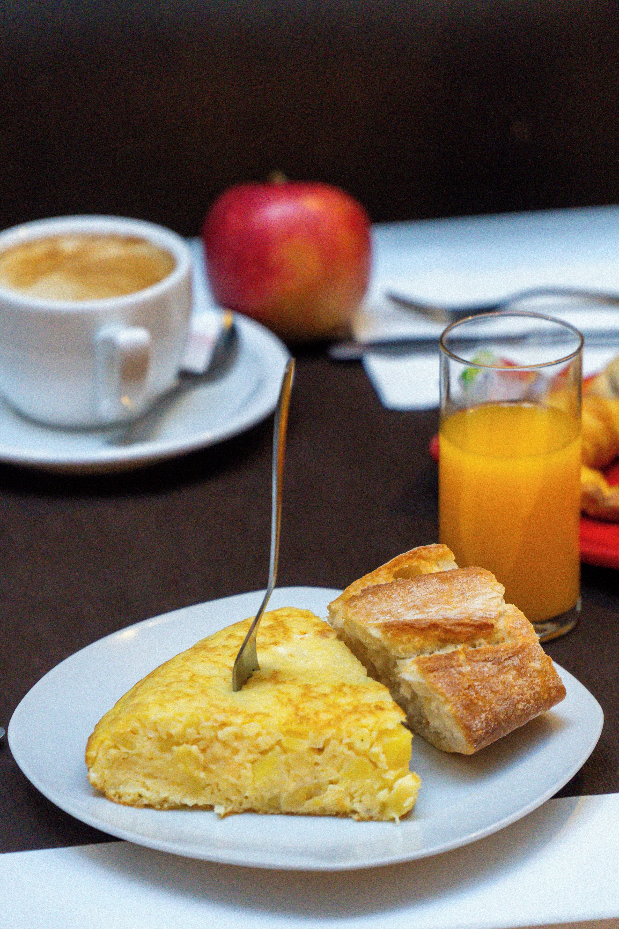 A breakfast plate with a slice of omelette, a glass of orange juice, and a cup of coffee on a table.