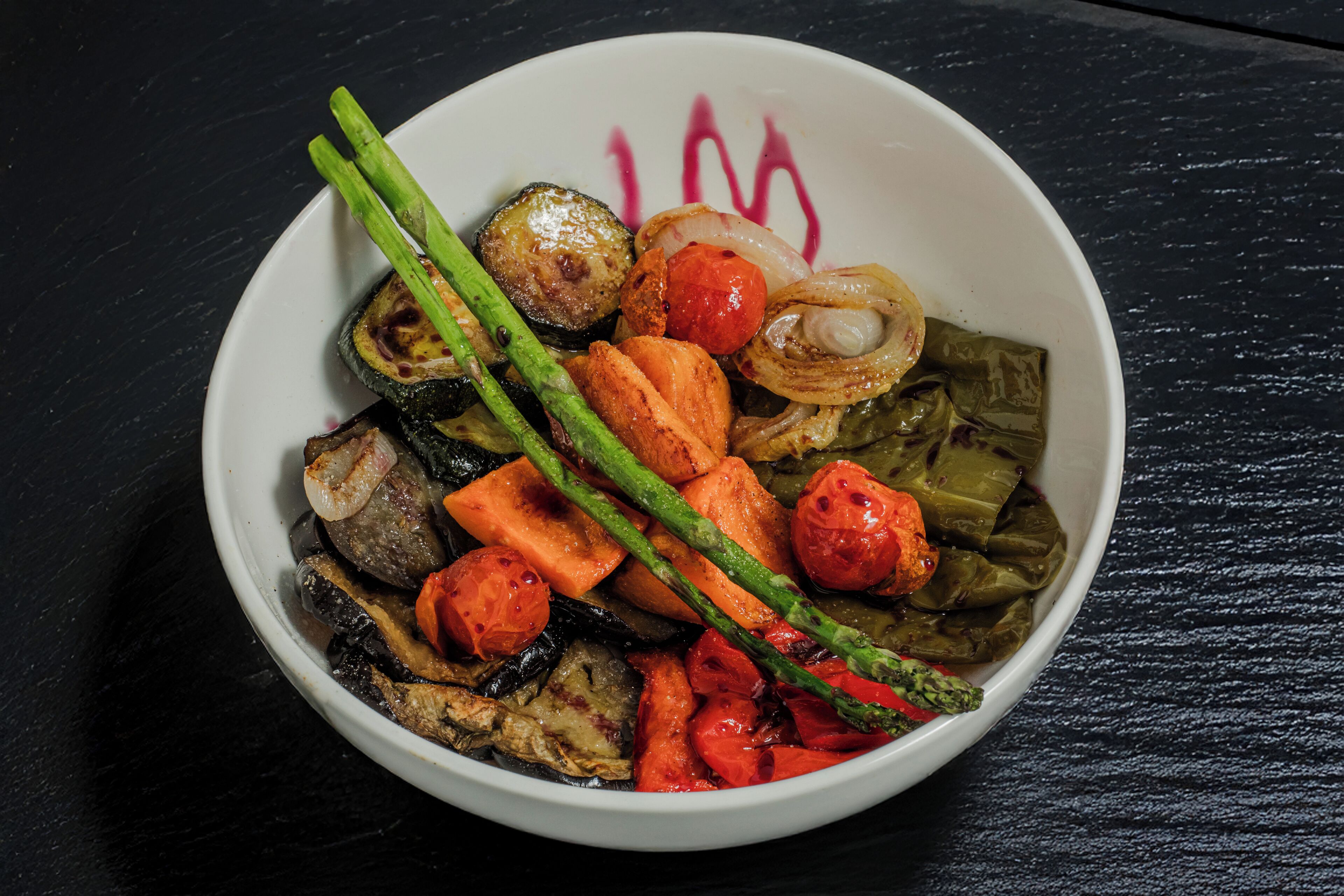 Un tazón de verduras asadas, entre ellas espárragos, tomates y cebollas.