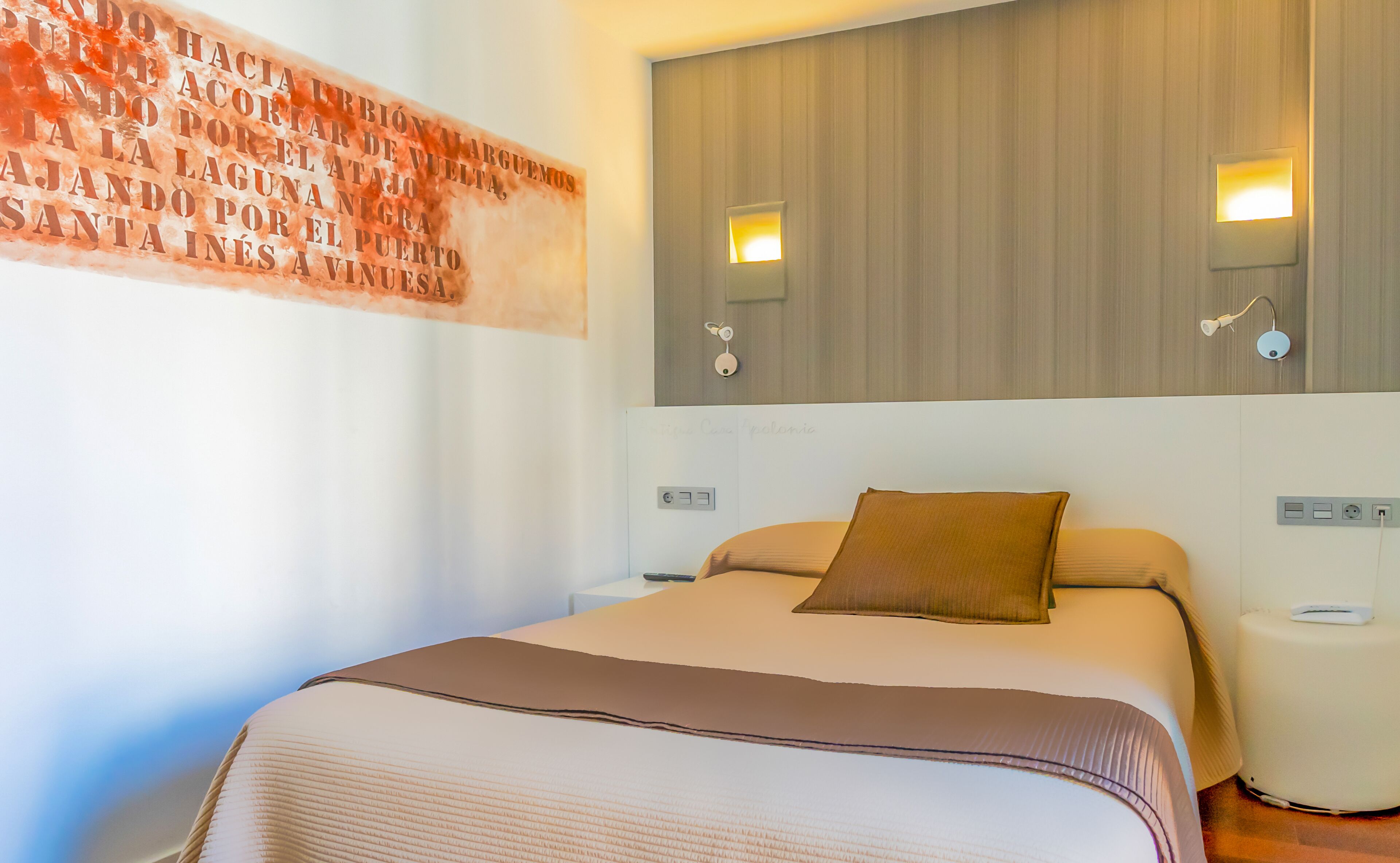 A hotel room with a large bed, two bedside tables, a wall-mounted light fixture, and a decorative wall piece.