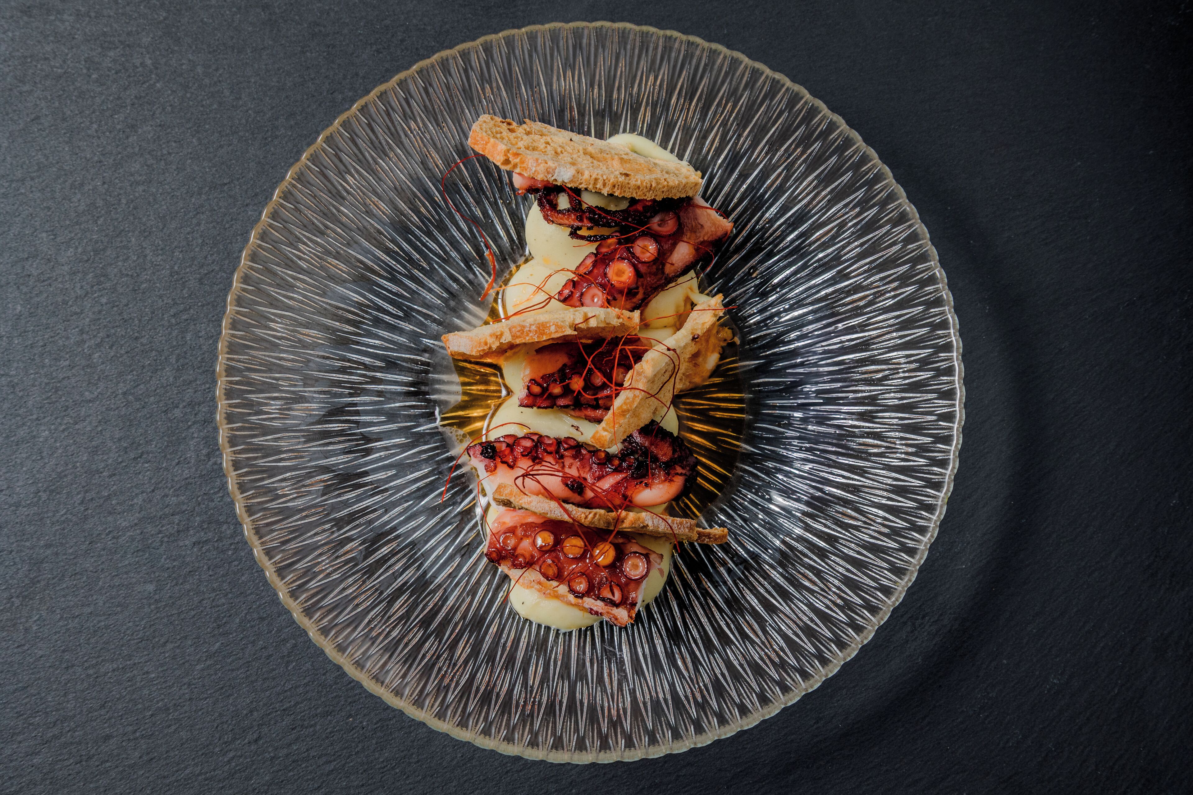 Un plato con pulpo, pan y salsa.