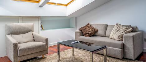 A modern loft bedroom with skylights, a sofa, a chair, and a glass coffee table.